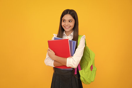 School teenage girl with school bag backpack hold book on yellow isolated studio background. Children school and education concept.の写真素材