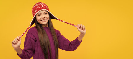 happy child in earflap hat. kid wear warm knitted clothes on yellow background. Banner of christmas child girl, studio kid winter portrait with copy space.の写真素材