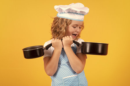 Kid chef cook with cooking pot stockpot. Cooking children. Chef kid boy making healthy food. Portrait of little child in chef hat isolated on studio background. Kid chef. Cooking process.の写真素材