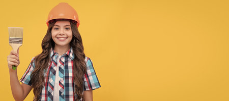 happy teen girl with curly hair in construction helmet hold painting brush, painting. Child builder in helmet horizontal poster design. Banner header, copy space.の写真素材