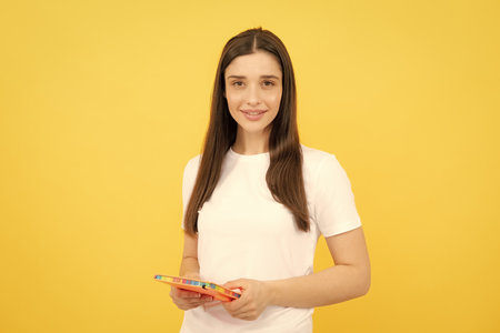 Female student holds books isolated on yellow background in studio. English language school, education concept.の写真素材