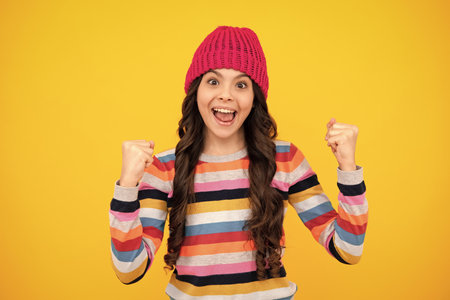 Amazed teenager. Modern teen girl wearing sweater and knitted hat on isolated yellow background. Excited teen girl.の写真素材
