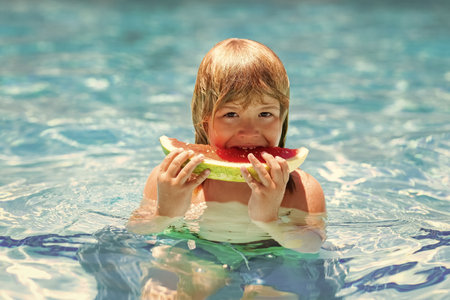 Child with watermelon in swimming pool. Kids eat summer fruit outdoors. Boy eating slice of red watermelon on the sea beach.の写真素材