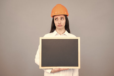 Young woman construction manager. Woman builder isolated portrait with protect helmet and board. Gray background, empty space, copy space.の写真素材