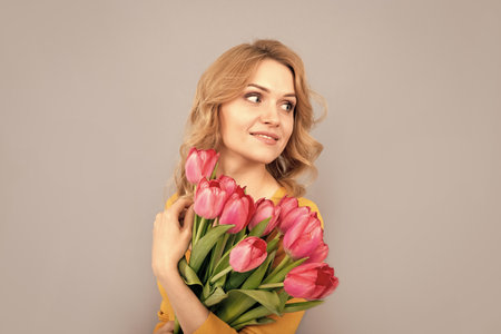 smiling woman with tulips on grey backgroundの写真素材