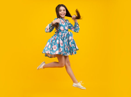Full length overjoyed teenager kid girl 12 13 14 year jumping old isolated on yellow background studio. Funny jump. Child in summer movement dress.の写真素材