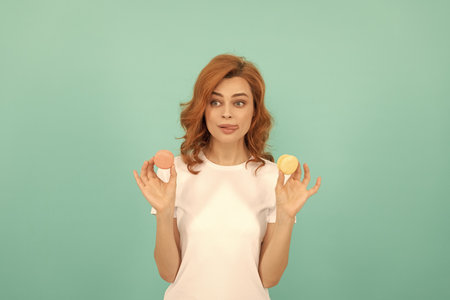 surprised woman hold sweet macaron french cookie on blue backgroundの写真素材