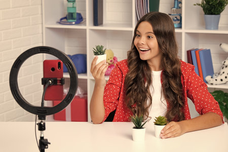 Teenager blogger making video, child vlogger influencer record content. Child blogger records video on mobile phone using ring lamp, video lights for blog or vlog at home. Happy smiling girl.の写真素材