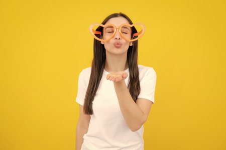 Cheerful girl in large funny party glasses sunglasses. Portrait of young woman wearing funny glasses isolated on yellow background.の写真素材