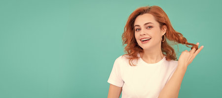 positive redhead girl with curly hair on blue background. Woman isolated face portrait, banner with copy space.の写真素材