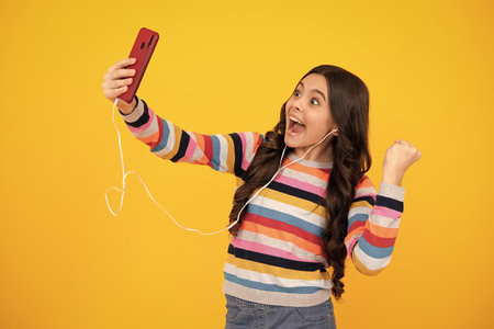 Kids selfie. Close-up portrait of cute teen girl using mobile phone, cell web app, isolated over bright vivid vibrant yellow color background. Happy teenager, positive and smiling.の写真素材