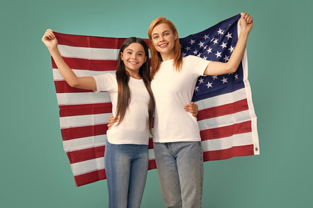 Patriotic holiday. Happy family, mother and daughter with American flag on blue isolated studio background. USA celebrate independence day 4th of July.の写真素材