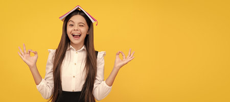Absorbing the knowledge. Happy school girl hold book on head making mudra gesture. Knowledge day. Portrait of schoolgirl student, studio banner header. School child face, copyspace.の写真素材