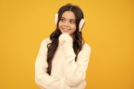 Teen girl wearing sweater and winter warm earmuff hat on isolated yellow background.の写真素材