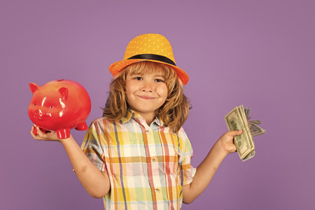 Saving money for travel. Cash money dollars bills and piggy bank concept. Portrait of a little boy putting money on a moneybox. Child saving money in a piggybank on background.の写真素材
