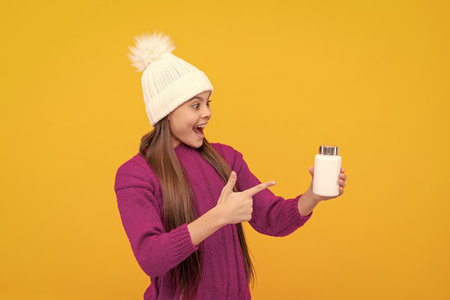 amazed kid in hat point finger on vitamins on yellow backgroundの写真素材