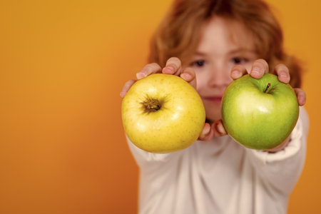 Close up kid with apple in studio, selective focus. Studio portrait of cute child hold apple isolated on yellow background.の写真素材