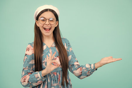 Positive teenager child points aside with cheerful expression, shows amazing at blank empty space. Advertisement and mockup. Happy teenager, positive and smiling emotions.の写真素材
