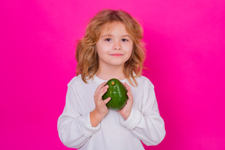 Child with avocado in studio. Portrait of cute child with avocado isolated on pink background.の写真素材
