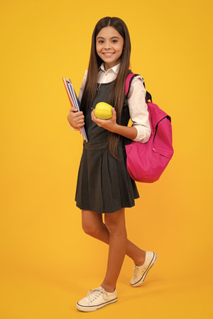 Schoolchild, teenage student girl with school bag backpack hold aplle and books on yellow isolated studio background. Children school and education concept.の写真素材
