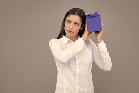 Sad pretty young woman holding gift box over gray background.の写真素材