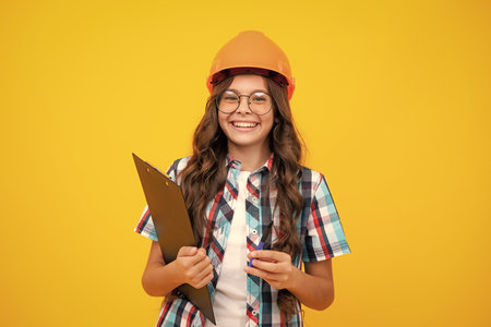 Teenager child painter in helmet with clipboard. Child in hard hat. Kid engineer on construction site. Renovation and repair.の写真素材