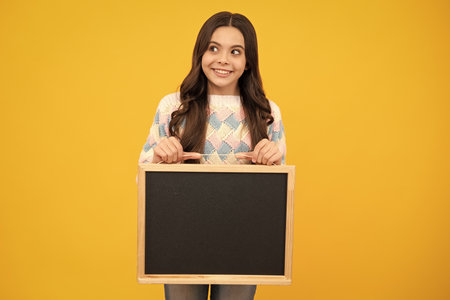 Teenage girl child hold chalkboard. Elementary school girl holding a blank blackboard chalk board. Copy space, mockup banner.の写真素材