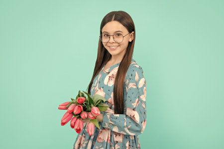 teen girl with spring bouquet on blue background. floral present. cheerful child in glassesの写真素材