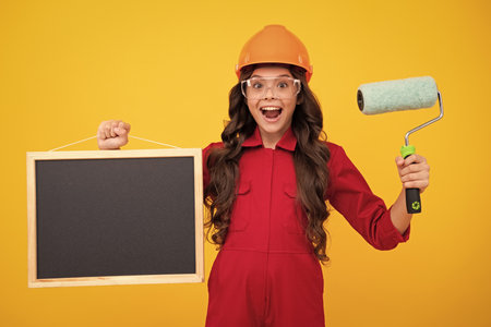 Blackboard for copy space. Excited teenager girl. Renovation for childrens room. Little girl in protective helmet and paint brush for painting walls.の写真素材