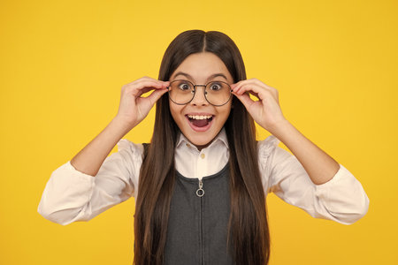 Cute school girl wearing glasses on yellow studio background, smart clever schooler girl in eyeglasses. Nerd student, genius schoolgirl, School, education concept.の写真素材