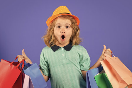 Discounts and sales. Happy child with shopping bags. Kid with shopping bags posing on blue studio isolated background. Trends.の写真素材