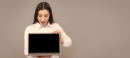 surprised woman in white shirt showing computer ad presentation, copy space, advert. Woman isolated face portrait, banner with mock up copy space.の写真素材