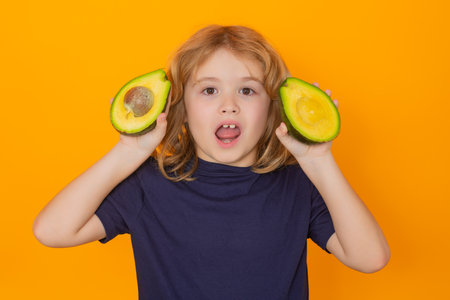Kid hold avocado in studio. Studio portrait of cute child with avocado isolated on yellow background, copy space.の写真素材