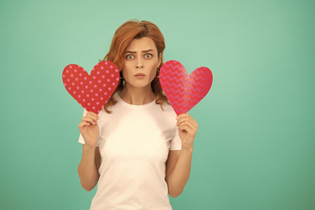 confused young lady with red heart on blue backgroundの写真素材