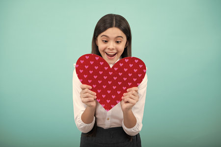 Excited face. Teenage girl hold shape heart, heart-shape sign. Child holding a red heart love holiday valentine symbol. Amazed expression, cheerful and glad.の写真素材