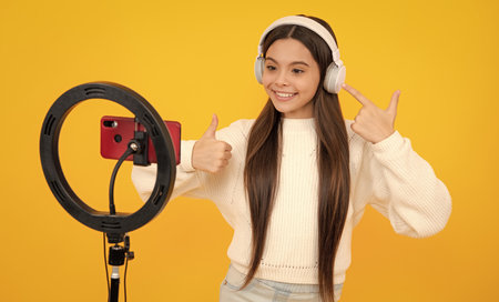 Teen girl speaking in front of camera for vlog isolated on yellow background. Teenager working as blogger, recording video blog.の写真素材