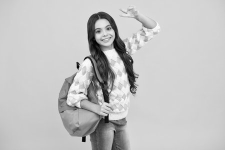 Schoolgirl in school uniform with backpack. Teenage girl student on yellow isolated background. Learning and education.の写真素材