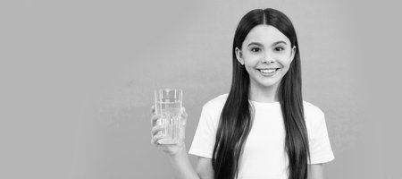 happy child going to drink glass of water to keep daily water balance, water balance. Banner of child girl with glass of water, studio portrait with copy space.の写真素材