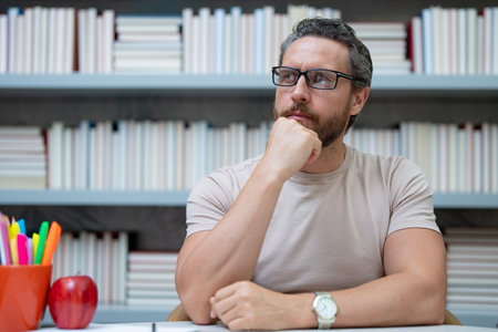 Portrait of teacher with book in library classroom. Handsome teacher in university library. Teacher giving classes. School teacher in library. Tutor at college library on bookshelf.の写真素材