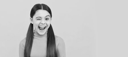 winking child with long hair on yellow background, emotions. Child face, horizontal poster, teenager girl isolated portrait, banner with copy space.の写真素材