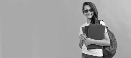 happy kid with backpack and copybook ready to study at school. Portrait of schoolgirl student, studio banner header. School child face, copyspace.の写真素材