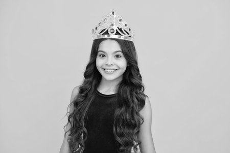 Teen child in queen crown isolated on yellow background. Princess in tiara. Prom party. Happy girl face, positive and smiling emotions.の写真素材