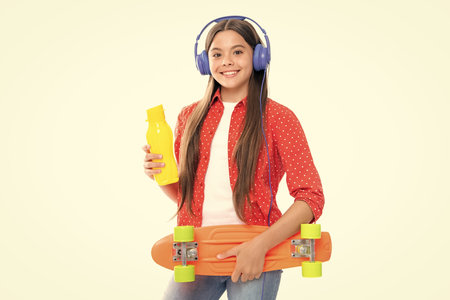 Studio shot of trendy teenage fashion model in casual look. Teenager youth hipster urban lifestyle. Child girl in street style with a skateboard and headphones.の写真素材