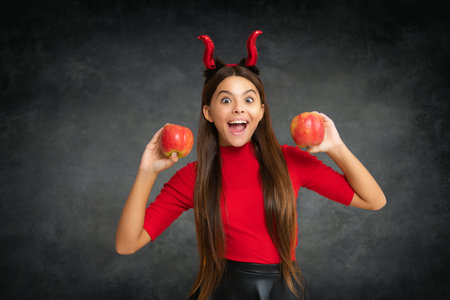 Halloween school. Happy Teen with devil horns hold apple. Halloween witch teen girl. Little girl...