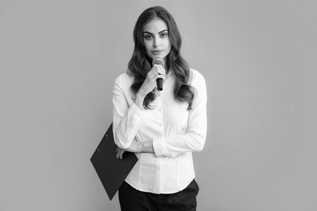 Young female journalist or businesswoman with microphone and clipboard on gray background.の写真素材