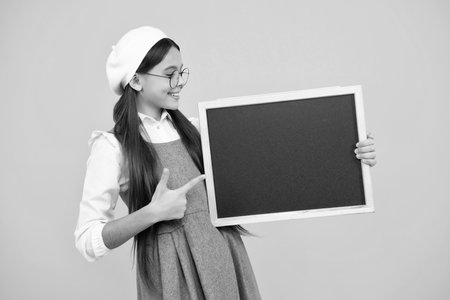 Teenager young school girl holding school empty blackboard isolated on yellow background. Portrait of a teen female student. Happy face, positive and smiling emotions of teenager girl.の写真素材
