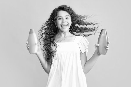Teenager child girl with bottle shampoo conditioners or shower gel. Kids hair care. Hair cosmetic product, shampoo bottle. Excited teenager, glad amazed and overjoyed emotions.の写真素材