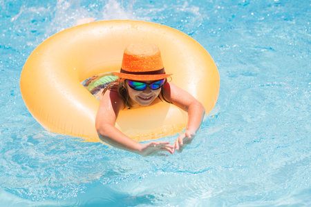 Child with inflatable ring in swimming pool. Kid boy swim in outdoor pool of tropical resort. Hot Summer. Water toys and floats for kids.の写真素材