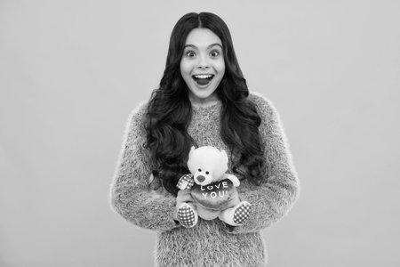 Teenager child girl in holding plush toy isolated on yellow background, happy childhood. Child with toy teddy bear with love heart for valentines day. Happy teenager, positive and smiling.の写真素材