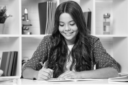 School student writing in exercise book, studying in classroom. Happy schoolgirl.